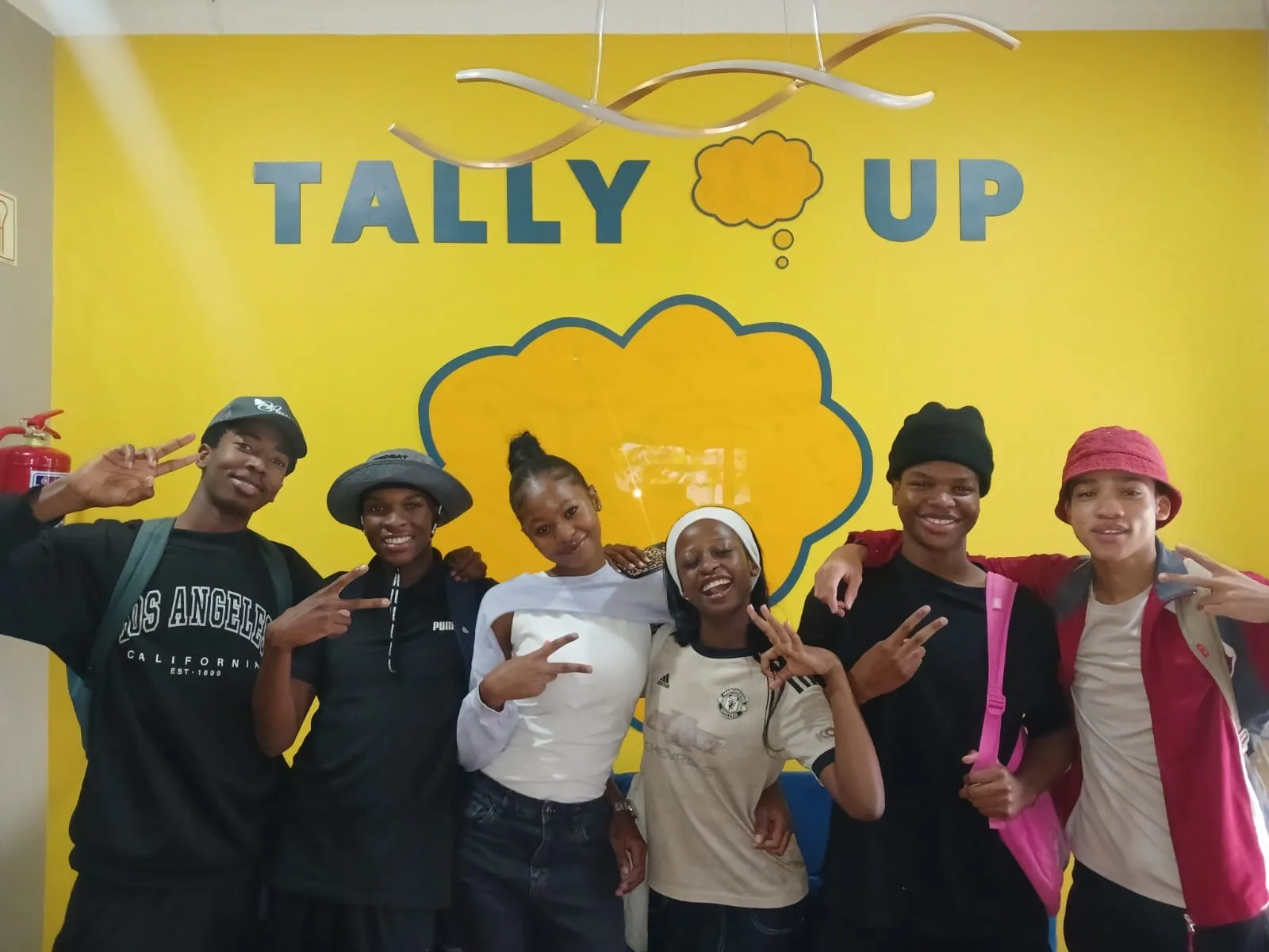 Tally Up learners in front of the yellow Tally Up wall